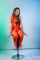 Wearing an orange suit, a cute girl model poses while sitting on a red chair