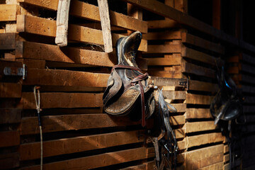 The brown saddle on the wooden stable door is a close-up. Worn saddle for horses made of genuine leather.