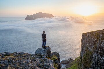 Gigure on the cliff. Amazing clouds over Mykines islands in sunset light, Faroe Islands
The Island of Mykines sits in the background with the early sunset like illuminating the clouds.