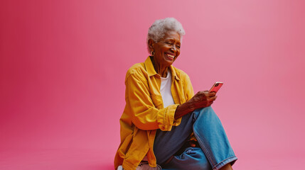 Joyful elderly woman with white hair smiling while using a smartphone, set against a vibrant pink background.