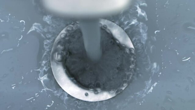 A close-up high-angle video captures the moment of clear water quickly flowing down a stainless steel drain in a bathroom sink.