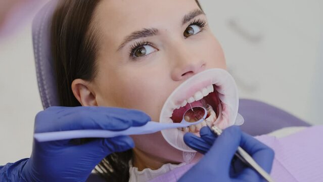 Dentist examines female patient mouth with dental instruments and optragate in private clinic. Professional dental checkup to maintain oral cavity health