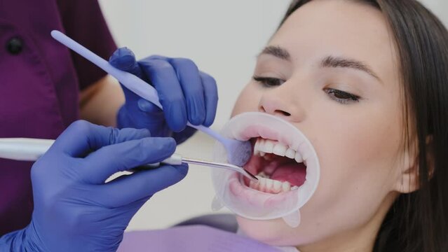 Female dentist blows air across teeth drying surface from saliva for further checkup. Dentist prepares for dental examination of oral cavity