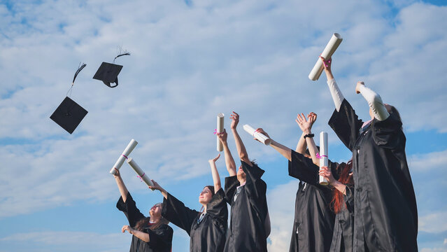 Happy college graduates tossing their caps up at sunset.