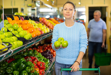 Positive middle-aged female buyer choosing organic granny smith green apples in hypermarket
