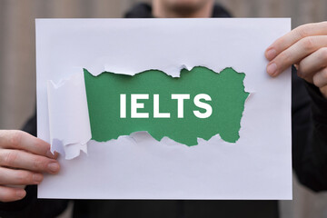 Man holding white and green sheets of paper with text: IELTS. Concept of IELTS International...