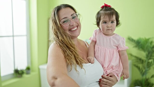 Confident mother, smiling in love, holding her happy child, standing together in the laundry room, arms flipped around daughter, spinning a clothespin, enjoying the casual household chore.
