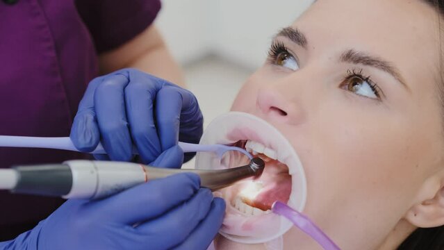 Dental professional carefully removes damaged area of tooth using drill tool. Young lady with optragate experiences tooth drilling procedure in clinic