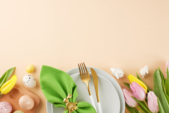 Joyful banquet creation: crafting a festive easter table. Top view shot of plates, cutlery, napkin, eggs, tulips, bunnies on beige background with space for festive message
