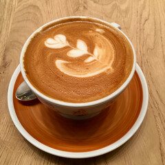 Cappucino coffee cup on wooden table. Romantic flower pattern. 