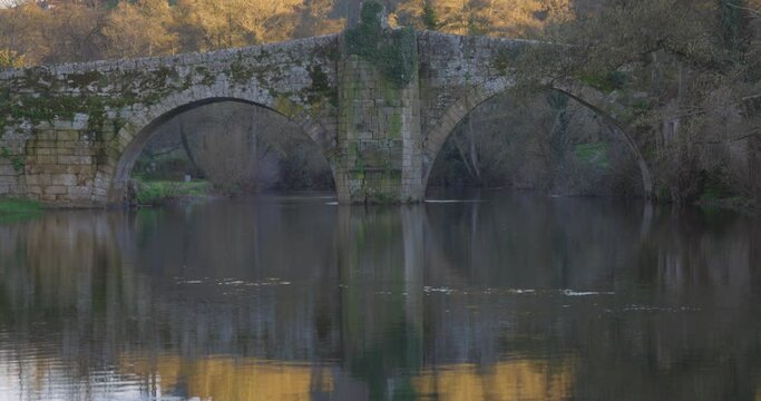 Medieval stone roman bridge over Arnoia river in Allariz with blurred people crossing in Galicia Spain