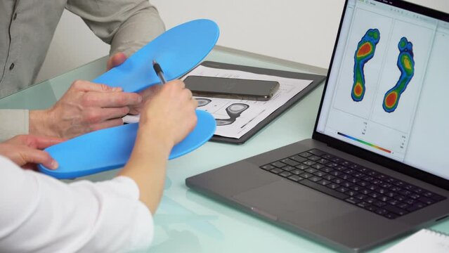 Doctor consulting male patient on custom orthotic insoles in a clinic for a personalised custom fitusing test picture on a laptop.