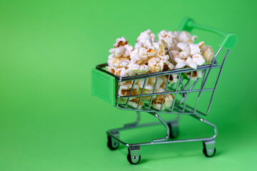 Freshly made popcorn in a shopping cart on green background