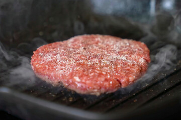Cooking burger beef patty on a hot frying pan close up. Preparing burger, homemade. Grocery product advertising, menu.