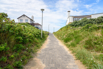 Empty footpath between two modern houses leading to a beach on a partly cloudy summer day - obrazy, fototapety, plakaty
