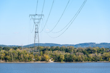 Tall electricity pylon supporting high voltage lines on the bank of a river on a sunny autumn day