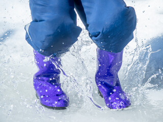 a boy jumps in a puddle, in rubber boots, snow, puddle, winter, sunny, spring, thaw