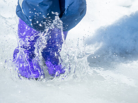 a child jumps in a puddle, in rubber boots, snow, puddle, winter, sunny, spring, thaw