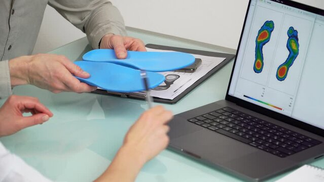 Doctor consulting male patient on custom orthotic insoles in a clinic for a personalised custom fitusing test picture on a laptop.