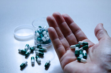 Close up of woman hand holding medicine pills and a jar with more pills behind.