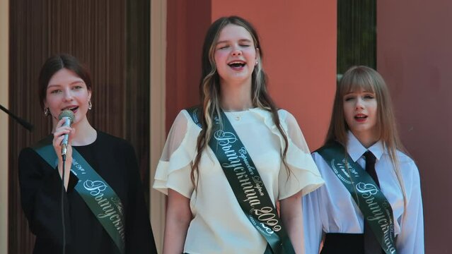 Belarusian schoolgirls sing at the graduation with a ribbon and the name - Graduate 2023 on it.