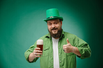 Bearded man with glass of beer showing thumb-up gesture on green background. St. Patrick's Day...