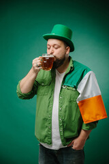 Happy bearded man with glass of beer and Irish flag on dark green background. St. Patrick's Day.