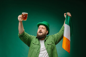 Happy bearded man with glass of beer and Irish flag on dark green background. St. Patrick's Day.