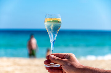 Hand with glass of cava or champagne sparkling wine on vacation, Dunes Corralejo sandy beach,...