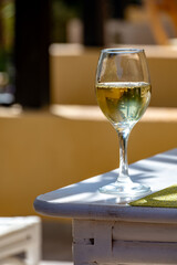 Glass of cold white wine on white terrace table outdoor in sunny day