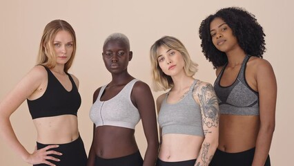 Cool fit sporty diverse young women wearing sportswear standing at beige background. Multicultural gen z girls multiethnic friends advertising sport fitness gym trainings together posing for portrait.