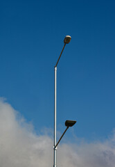 Postlamp with two symmetrical lamps in a city on a blue sky with clouds in the bottom. Symmetrical urban photography. Atmospheric image. 