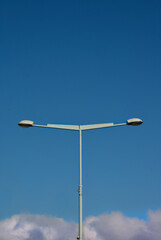 Postlamp with two symmetrical lamps in a city on a blue sky with clouds in the bottom. Symmetrical urban photography. Atmospheric image. 