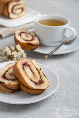 Roll with berry jam and chocolate whole and cut with a cup of tea on a light background. Close, free space.