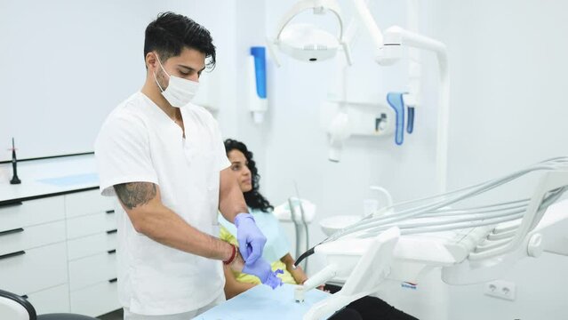 Male dentist putting on gloves before dental procedure. Stomatologist in white uniform and mask putting on latex gloves while preparing for teeth treatment of female patient