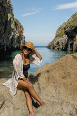 Beautiful young Latin woman, poses on a paradisiacal beach, wearing a white blouse and a straw hat