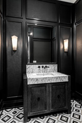 A bathroom with black wainscoting and wallpaper, a dark grey wood vanity cabinet, marble apron sink...