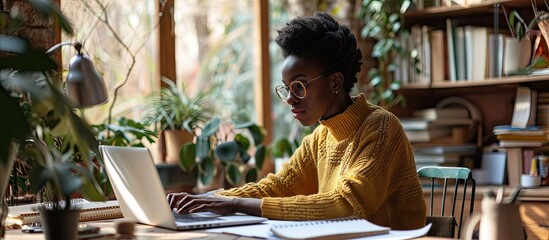 Smiling young black woman sitting at desk working on laptop taking notes in notebook happy millennial female study watching webinar using computer writing check list banner panorama free copy s