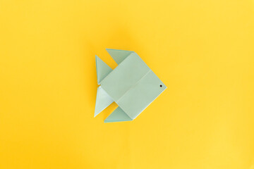 A blue origami fish with a drawn eye, set against a stark yellow background, perfect for an April...