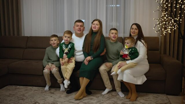 A large family sits on the couch at home and sings a Christmas carol
