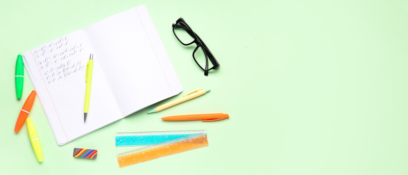 Copybook with maths formulas, glasses and stationery on light green background with space for text