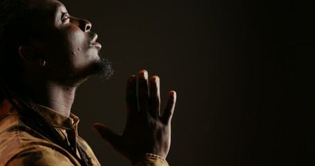 Religious adult believing in Jesus and praying in studio, showing belief and being hopeful over black background. Spiritual man feeling optimistic and talking to God. Handheld shot. Close up. - obrazy, fototapety, plakaty