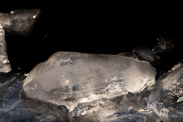 Close-up of fresh ice made from water. The ice was formed by rain and wind. It has many curves on the surface. The background is dark. The light refracts in the ice.