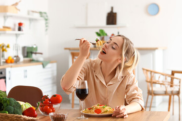 Young woman eating tasty pasta in kitchen