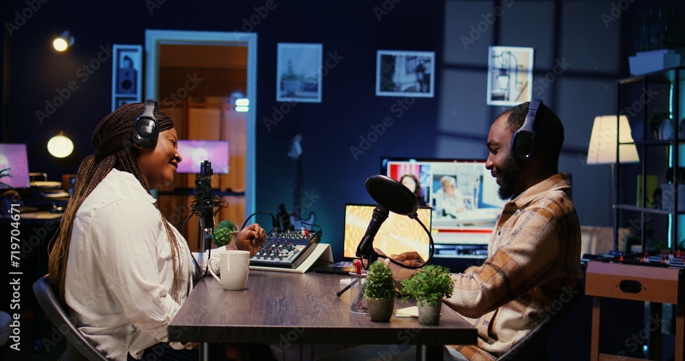 Poster vlogger show host adjusting analog mixer while talking with guest in neon lights ornate personal stu