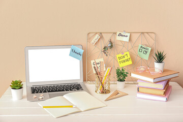 Laptop with sticky notes and stationery on table near beige wall