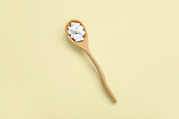 Wooden spoon with chewing gums on light yellow background