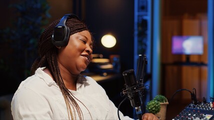 African american woman recording podcast, adjusting mic to ensure optimum sound quality for...