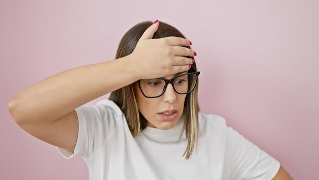 Oops! this young, beautiful hispanic woman wearing glasses, standing over isolated pink background, facepalms in regret - a classic blunder, forgetful hand to head moment!