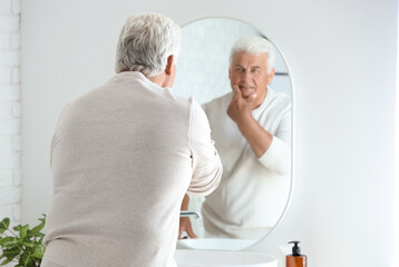Senior man looking in mirror at home, back view